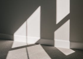 Shadow of window with glazing bars on wall and floor of minimal apartment in sunlight